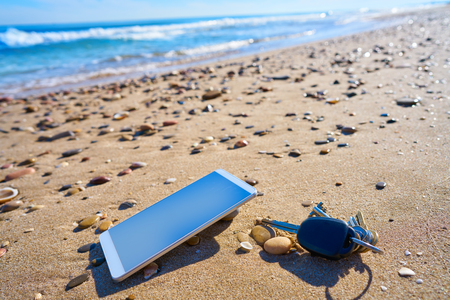 Mobile cell phone and car keys on beach sand as a Vacation metaphorの写真素材