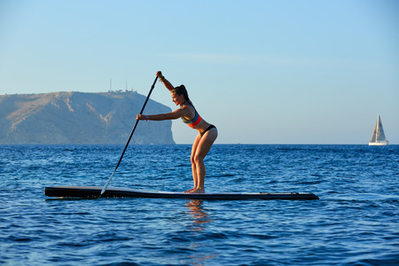 SUP Stand up Surf girl with paddle in a blue ocean seaの写真素材