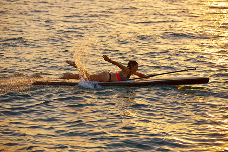 SUP Stand up Surf girl swimming lying on board at sunset