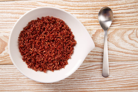 Red wild rice in a white plate over wooden boardの写真素材