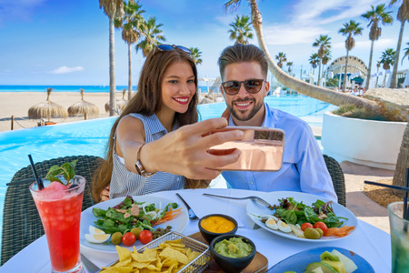 Young couple selfie smartphone photo in a swimming pool restaurantの写真素材