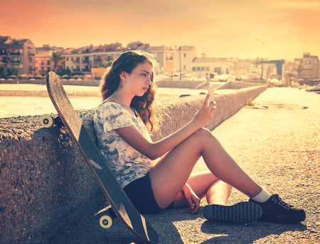 Roller Skate girl with smartphone sitting in a beach dock outdoorの写真素材