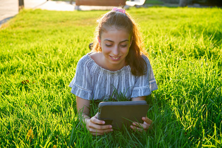 Girl lying in park  playing with tablet pc on lawn backgroundの写真素材