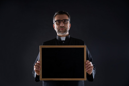 Priest holding empty blackboard copy space isolated on blackの写真素材