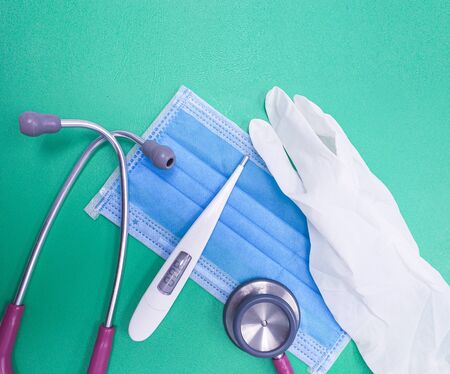 Closeup Medical equipment, gloves, blue surgical mask, stethoscope and thermometer Placed on a green...