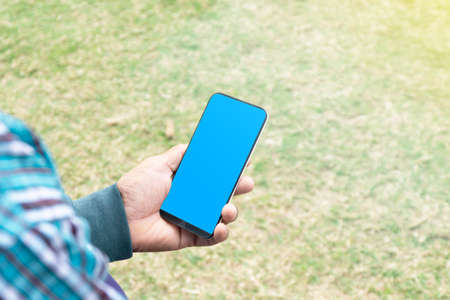 Hand holding phone with the blue color in front of a floor background,Smartphone in hand with a green chromakey screen.の写真素材