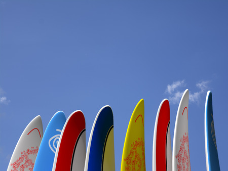 A set of surf boards vertically positioned with a blue sky and some clouds on the backgroundの写真素材