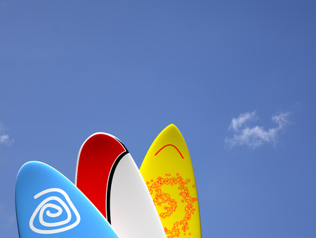 A set of surf boards vertically positioned with a blue sky and some clouds on the backgroundの写真素材