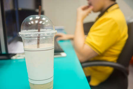 Plastic coffee cup on the background of people working with computers.の写真素材