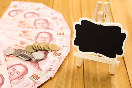 Images of banknotes and coins of 100 baht in Thailand and blackboard.On wood background.の写真素材