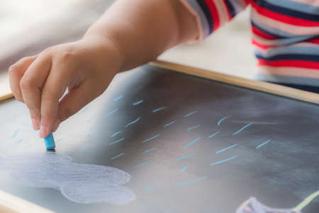 The girl kid holding green chalk in hand. She has a funing time learning to draw on blackboard or chalkboard at school.の写真素材