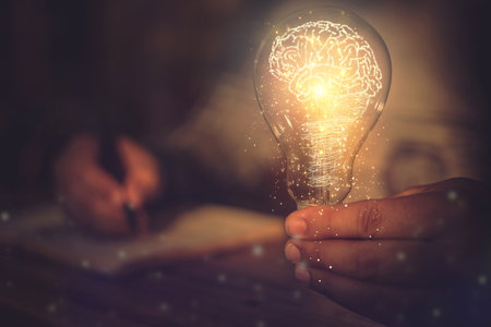 A young man's hand is holding a light bulb and his other hand is taking notes. in the concept of learning, studying and taking notesの写真素材