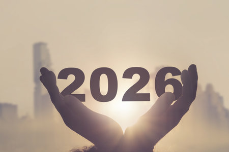 A pair of hands holding the number 2026 in front of the rising sun with a blurred city skyline in...