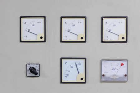 A set of analog ammeters and voltmeters mounted on an electrical panel. This image represents classic industrial technology, used for monitoring and controlling power systems with a visual, easy-to-read interface.の写真素材