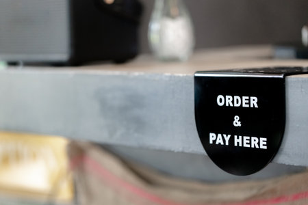 Black sign with white text order and pay here attached to counter in cafe, showing direction for customer service and payment area.の写真素材