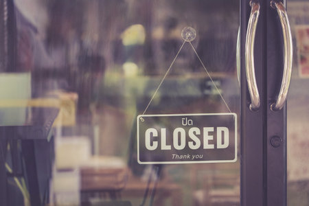 Close-up of closed sign hanging on glass door with reflection of cafe interior, representing store...