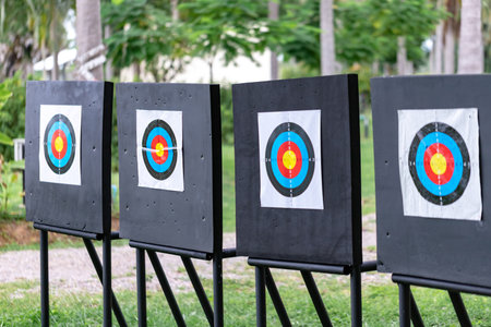 A well-organized outdoor archery range showing four targets set in a neat row. One of the targets has a visible arrow successfully hitting the center (bullseye), symbolizing success, training progress, and multiple goals.の写真素材