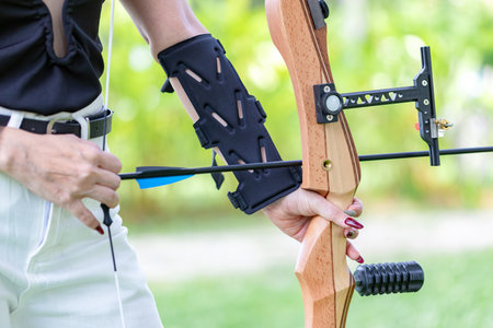 Close-up shot of a female archer's hands nocking an arrow onto a beautiful wooden recurve bow....