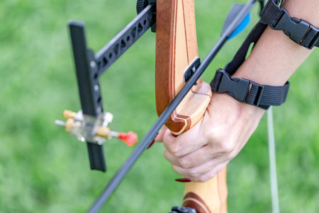 Detailed view of a hand holding the wooden riser of a modern recurve bow, with an arrow set on the...