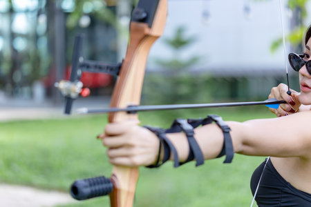 A bright, side-view shot of a cheerful female archer in modern gear and sunglasses, focused on the...