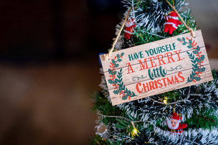 A charming close-up of a rustic wooden sign with a classic Christmas greeting, "Have Yourself a Merry Little Christmas," adorning a holiday tree with ornaments and lights. Ideal for seasonal advertisingの写真素材