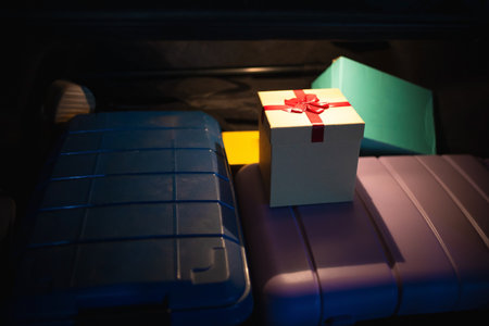 Holiday gift-wrapped box and multiple pieces of colorful luggage packed in the trunk of a vehicle. A conceptual image for last-minute Christmas shopping, gift delivery, or the start of a New Year's travel planの写真素材