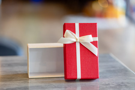 A neatly opened red and white gift box with a ribbon and bow, positioned on a gray table. The separated lid and empty bottom box are ideal for showcasing products or promotional contentの写真素材