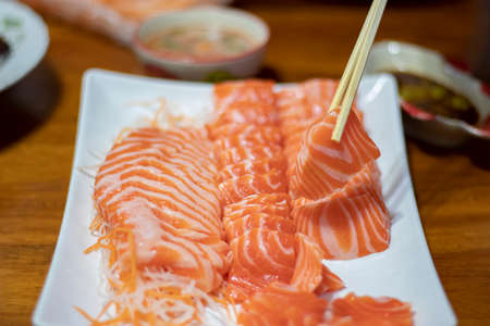 The hands were holding the chopsticks to hold the salmon sashimi, with copy space.の写真素材