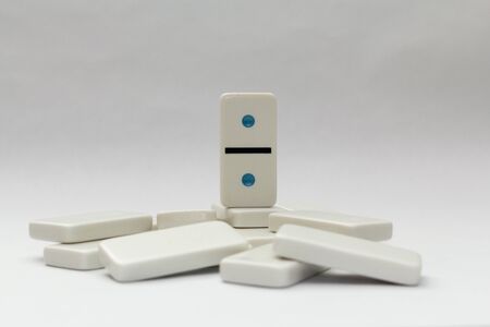 One colourful domino stand atop of fallen white dominos on a white background.の写真素材