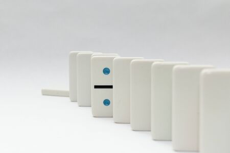 Line of white dominos on white background with last one fallen. One domino stands out from the crowd independent.の写真素材