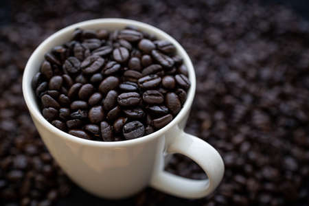 Roasted coffee beans in a white cup with beans in the background.の写真素材
