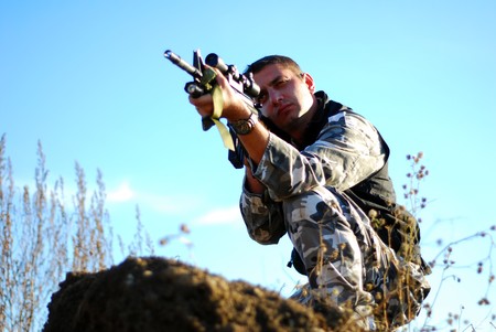 Soldier in camouflage aiming with his rifle outdoor