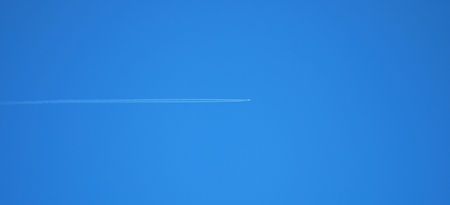 Passenger jet plane on clear, blue sky. Vapor traces parallel to the image edge. 