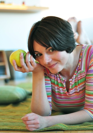 Portrait of happy young woman eating an apple on floor at homeの写真素材