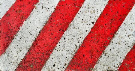 Diagonal red-white lines paint pattern on a rough textured cementの写真素材