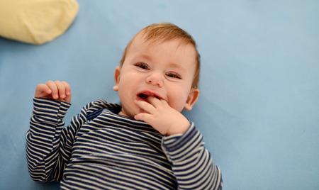 beautiful blue eyed baby kid crying and biting his fingersの写真素材