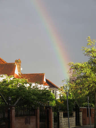 Rainbow with a dark overcast sky above suburban houses in London, Englandの写真素材