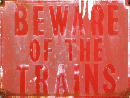 Old vintage red retro distressed railway enamel metal sign with text, beware of the trainsの写真素材
