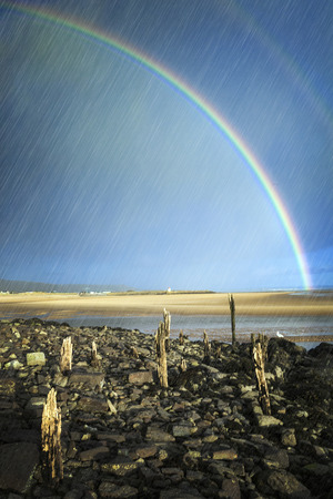 Rainbow and rain over the coastline beach at Burry Port Carmarthenshire Wales UKの写真素材