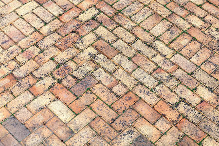 Stone wall background off old weathered distressed red brown brick with a herring bone paving...