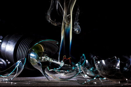 amazing explosion of a burning light bulb with splinters and smoke on a black background with a flashの写真素材