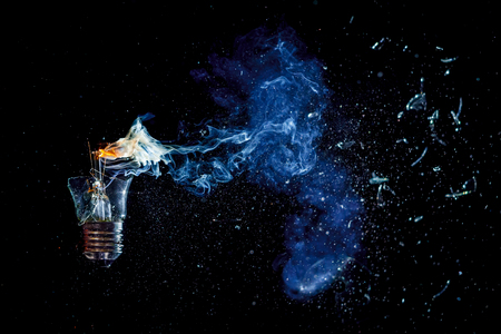 cosmic explosion of a burning light bulb with flying splinters and smoke on a black background with a flashの写真素材