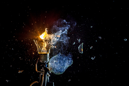 cosmic explosion of a burning light bulb with flying splinters and smoke on a black background with a flashの写真素材