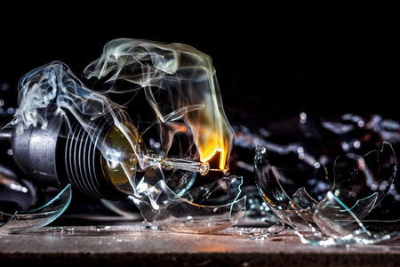amazing explosion of a burning light bulb with splinters and smoke on a black background with a flashの写真素材