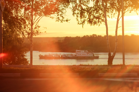 Deep morning dawn with highlights in the orange rays of the summer sun on the road against a grove of trees and a river on a blurred background in the light and shipの写真素材