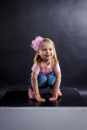 Portrait of cute European little blonde girls in jeans and pink t-shirt with the inscription: "Dad's pride, mom's joy", on a black isolated backgroundの写真素材