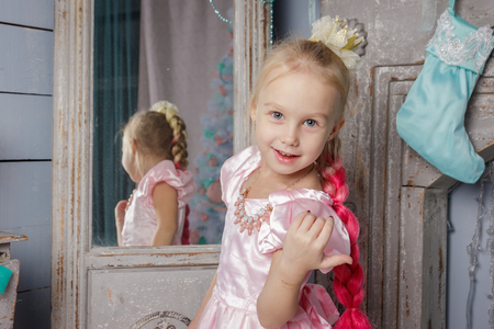 Portrait of cute european little blonde princess girl with crown in beautiful dress in decorated studio in christmas location with toys and christmas treeの写真素材