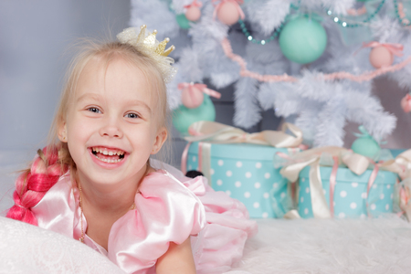 Portrait of cute european little blonde princess girl with crown in beautiful dress in decorated studio in christmas location with toys and christmas treeの写真素材