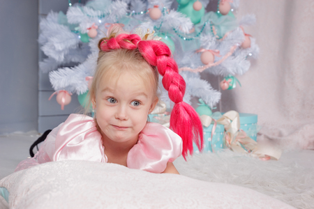 Portrait of cute european little blonde princess girl with crown in beautiful dress in decorated studio in christmas location with toys and christmas treeの写真素材