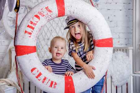 Portrait of two cute and naughty european little girls in sailors clothes in sea style studio on white brick wall backgroundの写真素材